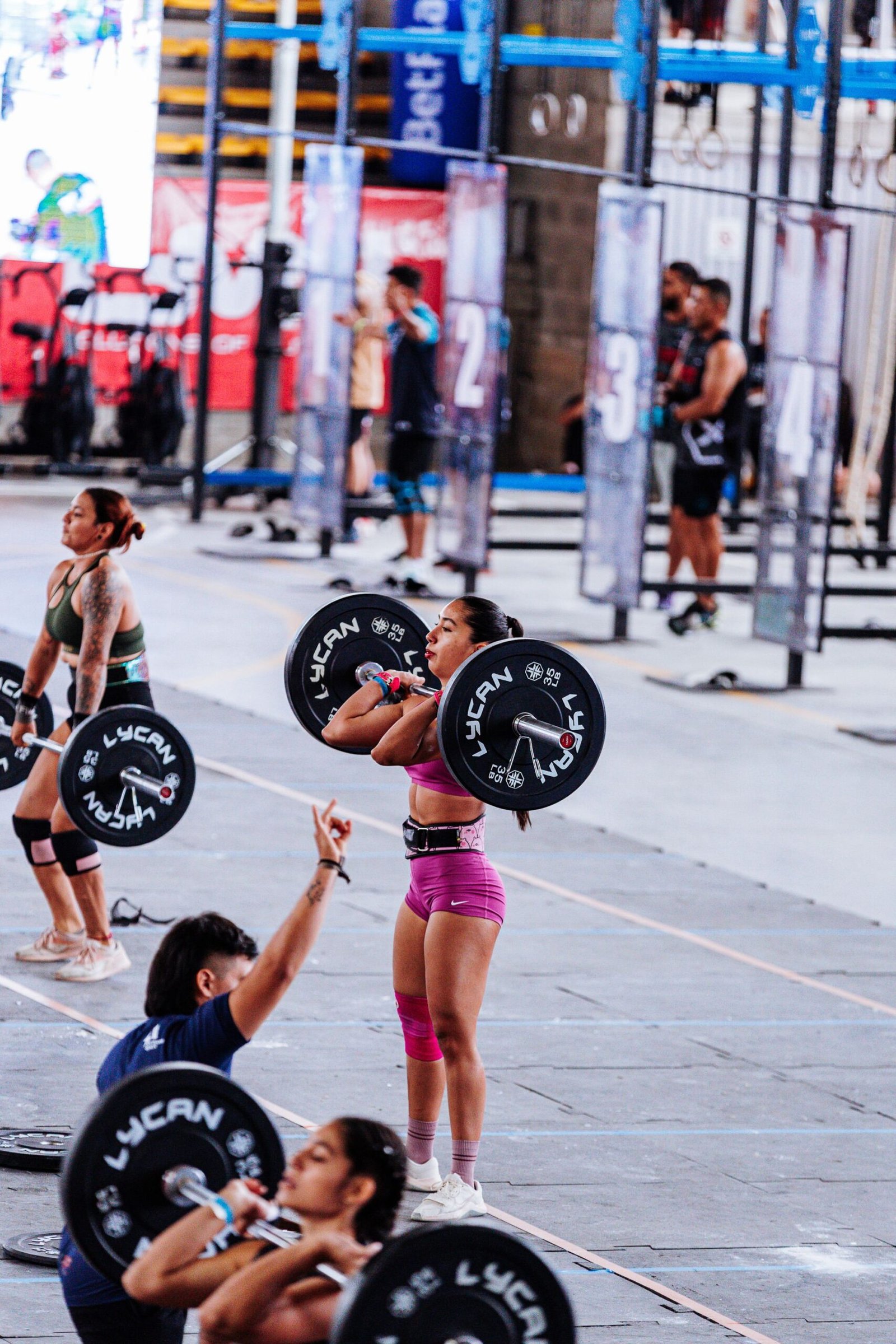 Female athletes lifting weights in a CrossFit competition, showcasing strength and determination.